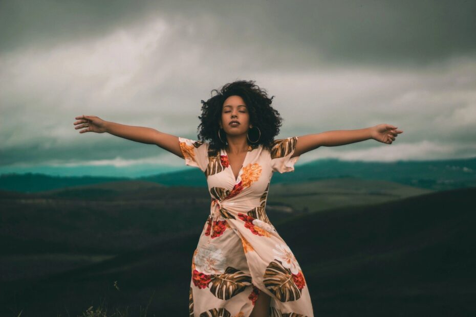 woman standing in nature with her arms spread wide as if at peace. Clouds can be seen rolling in, in the background.